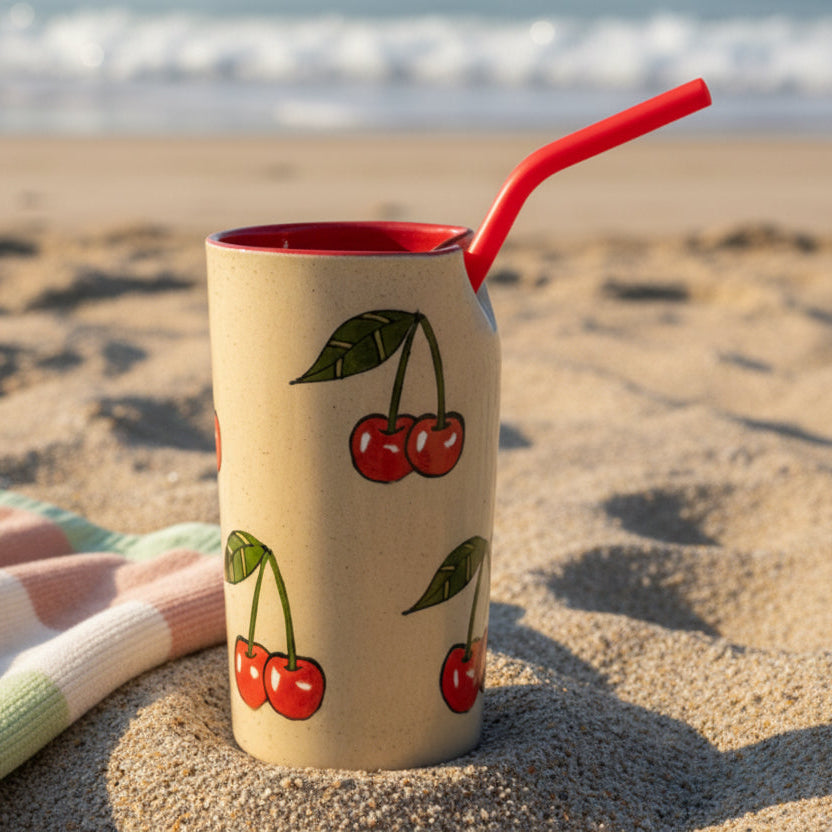 A ceramic cup with a cherry pattern, mounted on a gray wooden wall next to a white paneled wall, with a red straw protruding from the side.