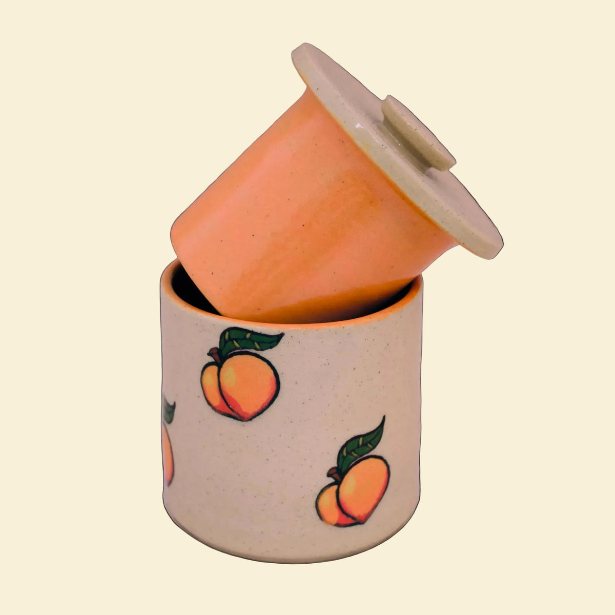 A speckled beige ceramic butter bell with a matching lid, decorated with a pattern of orange peaches with green leaves, set against a neutral light gray background.