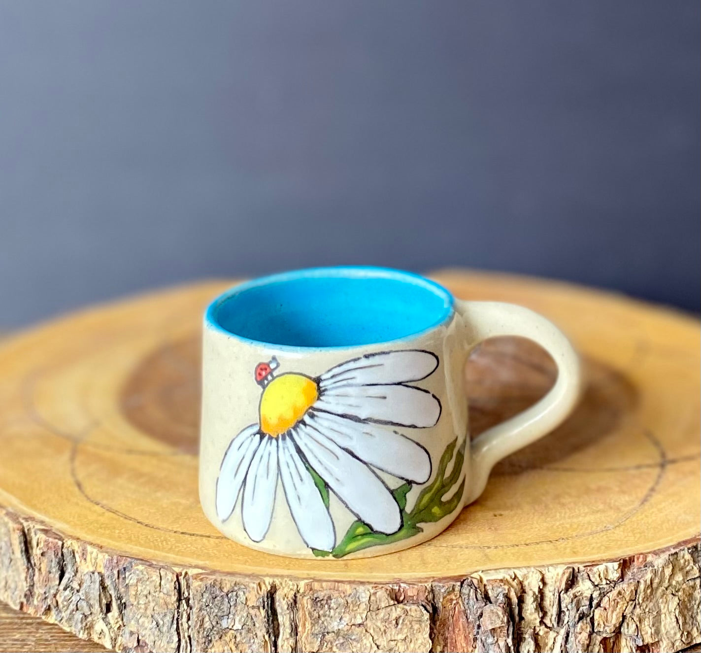 A hand-painted ceramic espresso mug with a floral pattern, featuring a daisy design and a ladybug, on a wooden surface.