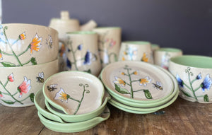 whimsical spring flowers and bees hand painted on a collection of hand made functional pottery. Ceramic art and made in penticton bc at the cannery trade centre, sold at the penticton farmers market